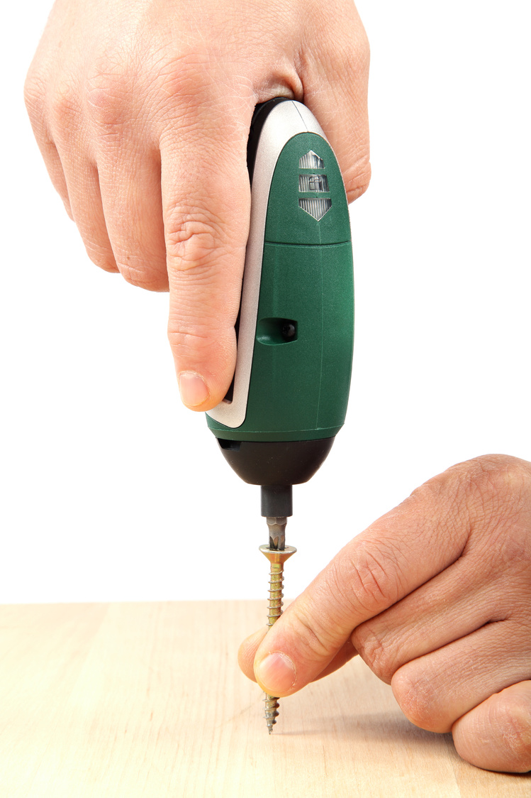 Hand with screwdriver screw spins in a wooden board.